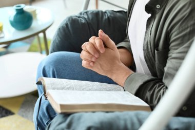 İncil 'i olan genç adam evde dua ediyor.