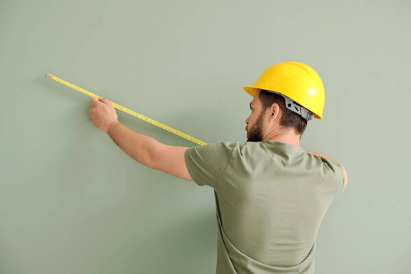 Male worker with tape measure on color background
