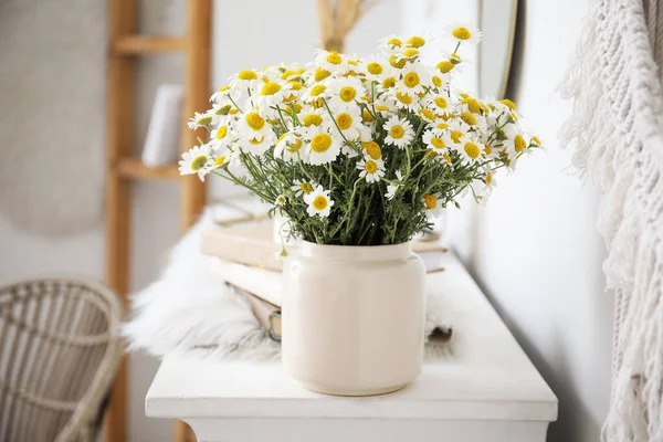 Vase with beautiful chamomiles on fireplace in room