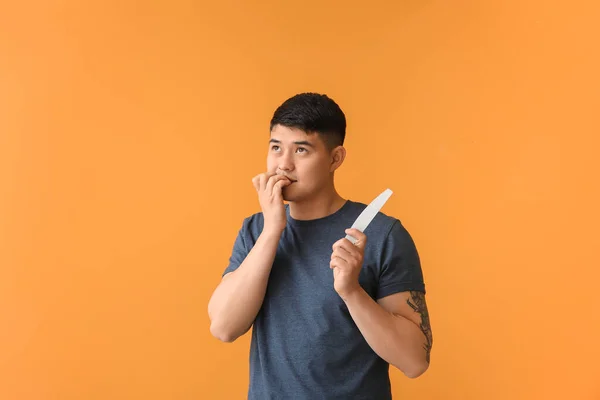 Asian man doing manicure on color background