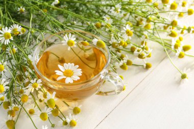 Beyaz ahşap arka planda bir fincan papatya çayı.