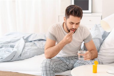 Genç adam yatak odasında uyku hapı alıyor.