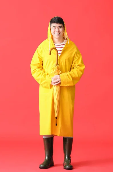 Young Asian man in raincoat on color background
