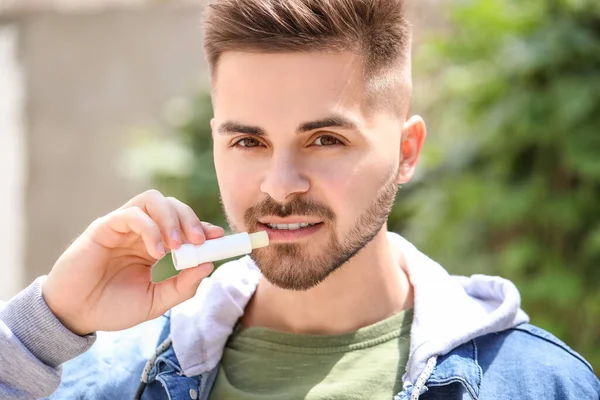 Handsome young man with lip balm outdoors