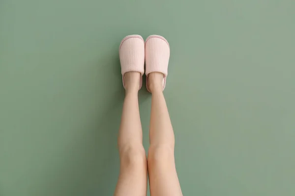 Female legs in soft slippers on color background