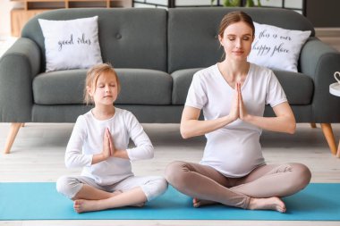 Genç hamile kadın ve küçük kızı evde yoga yapıyorlar.