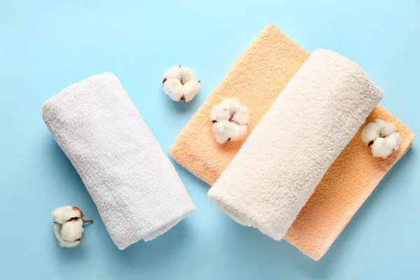 Cotton flowers and soft towels on color background