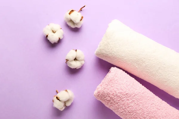 Cotton flowers and soft towels on color background