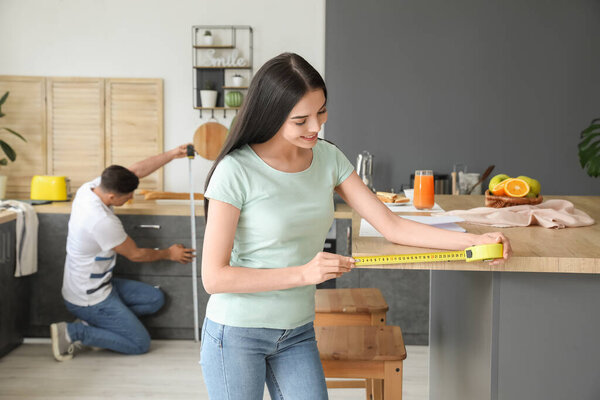 Молодая женщина принимает меры стола на кухне
