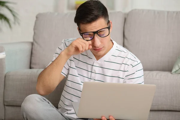 Young man suffering from sleep deprivation with laptop at home