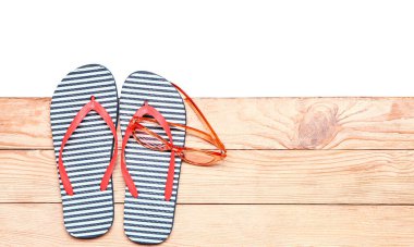 Tahta zeminde beyaz arka planda terlikler ve güneş gözlükleri