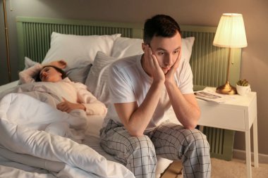 Young irritated man in bed with snoring wife clipart
