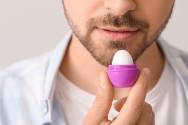 Hafif arka planda dudak kremi olan yakışıklı genç adam, yakın plan.