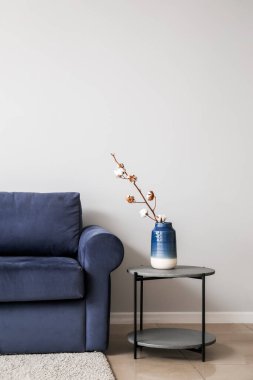 Şık bir kanepe ve odada ışık duvarı yanında pamuk çiçekleri olan bir masa.