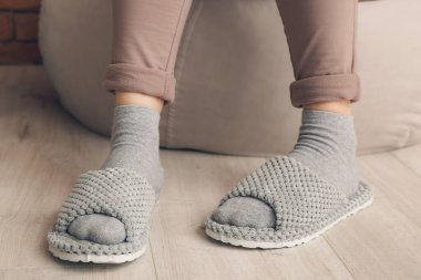 Yumuşak terlikli bir kadın evde puf üzerinde oturuyor.