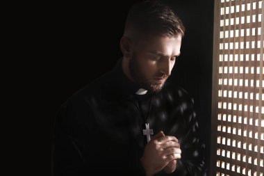 Young priest in confession booth clipart