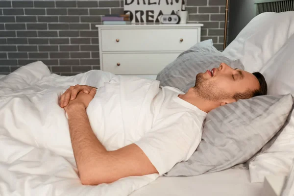 Young man snoring while sleeping in bed. Apnea problem