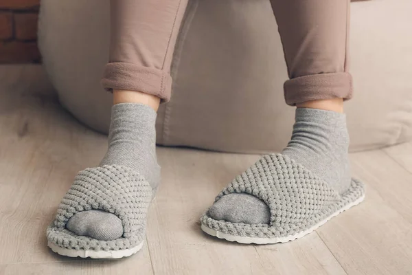 Woman in soft slippers sitting on pouf at home