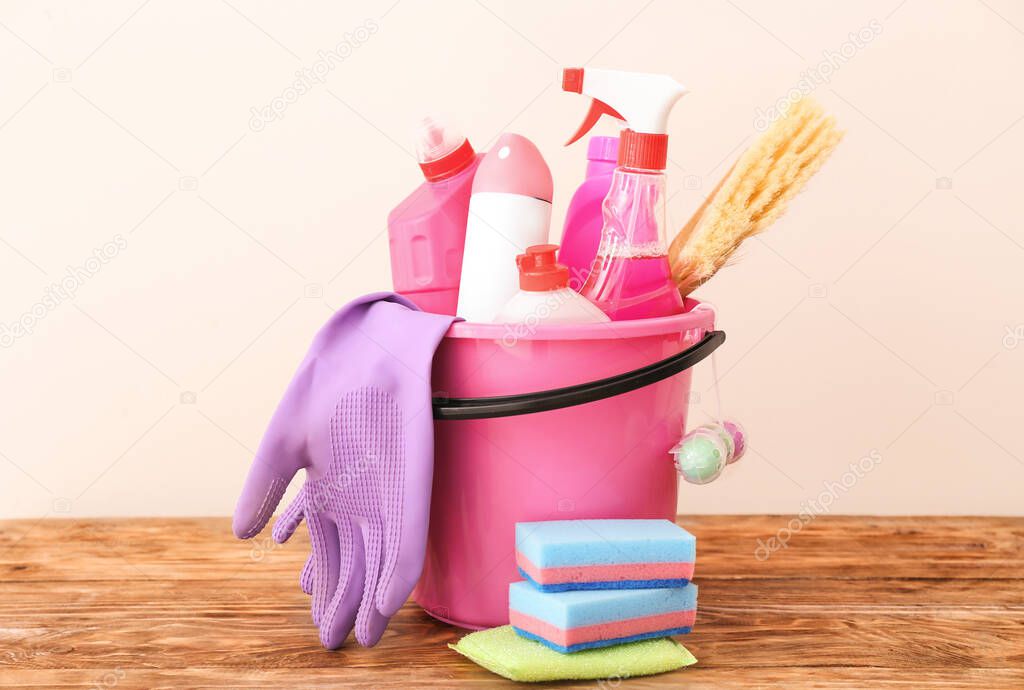 Bucket with set of cleaning supplies on table