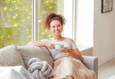 Güzel, genç, Afro-Amerikan kadın evde sıcak çay içiyor.