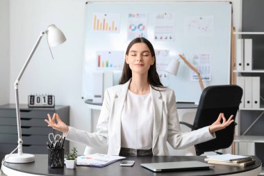 Genç iş kadını ofiste meditasyon yapıyor.