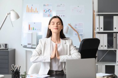 Genç iş kadını ofiste meditasyon yapıyor.