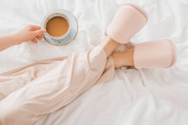 Yumuşak terlikli bir kadın yatak odasında kahve içiyor.