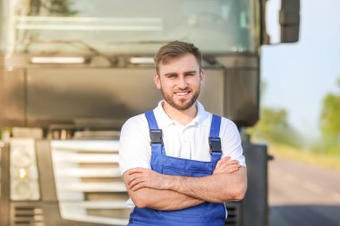 Dışarıdaki büyük kamyonun yanında bir erkek sürücü.