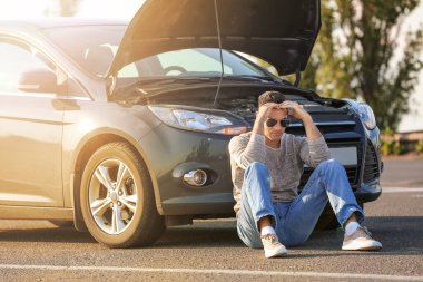 Yoldaki kırık arabanın yanındaki genç adam.