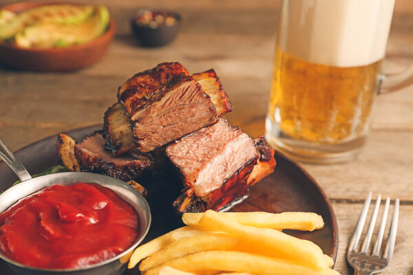 Tasty beef short ribs with sauce, french fries and beer on table