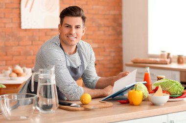 Yemek tarifi kitabıyla mutfakta limonata hazırlayan genç adam.