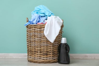 Kirli elbiseli sepet ve renkli duvarın yanında deterjan.