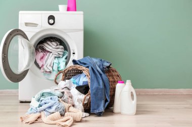Renkli duvarın yanında kirli çamaşırları olan çamaşır makinesi.