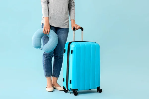 Woman with packed suitcase and travel pillow on color background