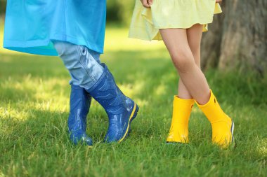 Parkta yağmurluk ve çizme giyen şirin çocuklar.