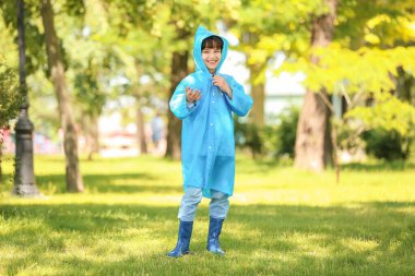 Parkta yağmurluk giyen şirin bir çocuk.