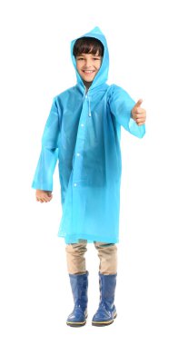 Beyaz arka planda baş parmağını gösteren yağmurluk giymiş şirin bir çocuk.