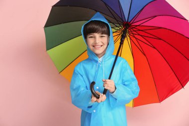 Yağmurluk giymiş şirin bir çocuk ve arka planda şemsiyesi var.