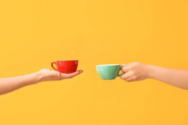 Hands with cups of hot coffee on color background clipart