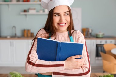 Mutfakta yemek tarifi kitabı olan genç bir kadın.