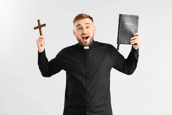 Überraschter Junger Priester Mit Bibel Und Kreuz Auf Hellem Hintergrund — Stockfoto