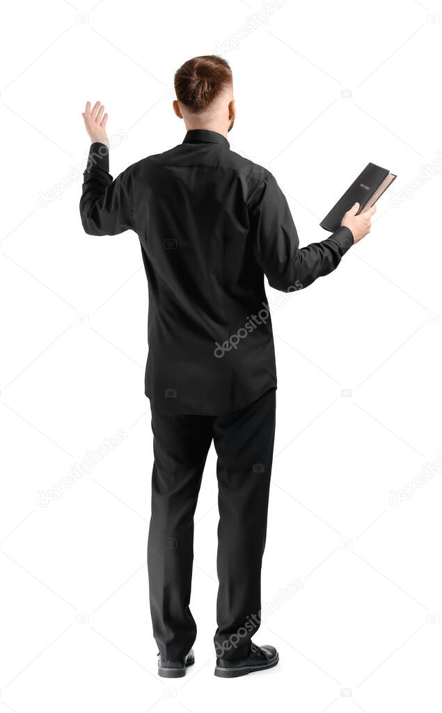 Handsome young priest with Bible on white background