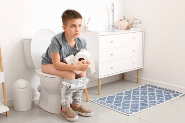 Tuvaletteki klozette oturan küçük çocuk.