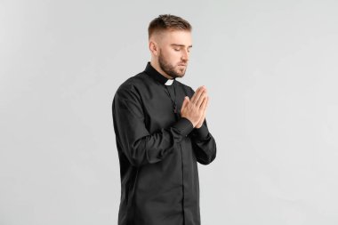 Young priest praying to God on light background clipart
