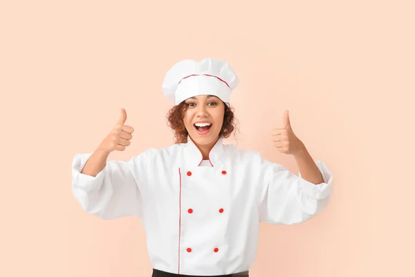 Female African-American chef showing thumb-up on color background