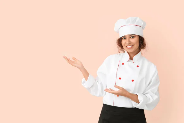 Female African-American chef showing something on color background