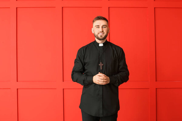 Handsome young priest on color background