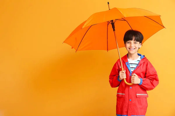 雨のコートと色の背景に傘でかわいい男の子 — ストック写真