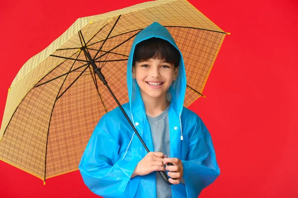 雨のコートと色の背景に傘でかわいい男の子 — ストック写真