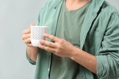 Gri arka planda çay fincanı olan yakışıklı genç adam, yakın plan.